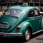Táxi Volkswagen Fusca verde circulando por uma rua movimentada de São Paulo.