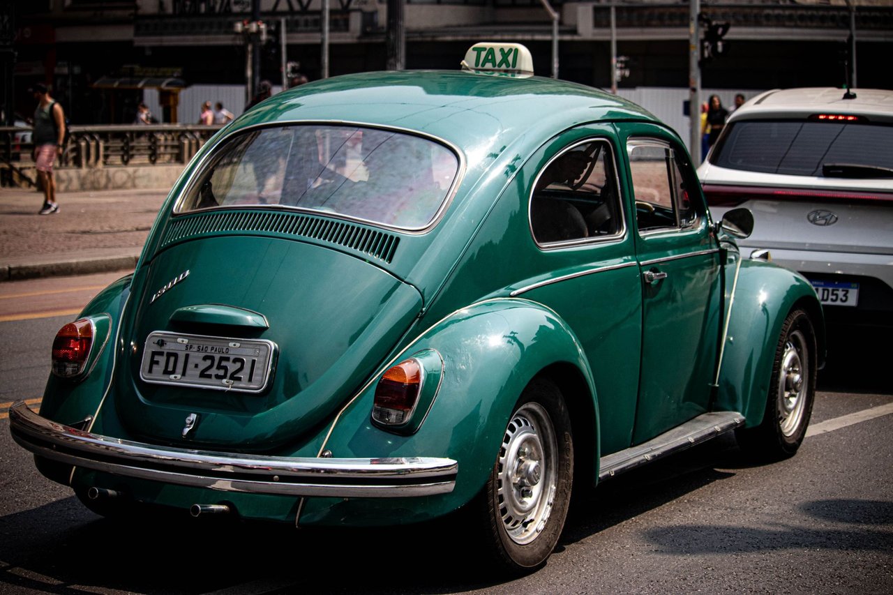 Táxi Volkswagen Fusca verde circulando por uma rua movimentada de São Paulo.